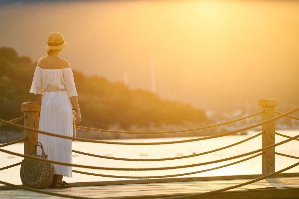 穿著白洋裝的女生站在海邊碼頭，望向夕陽，象徵自我療癒與感情的釋放（台灣氛圍）